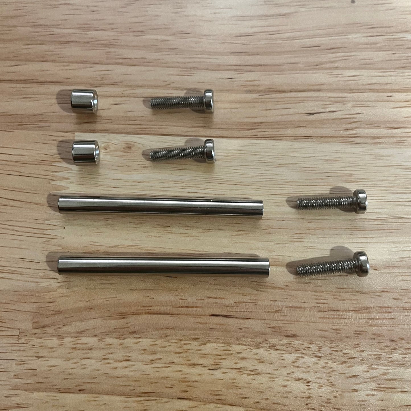 Set of metal screws used to secure acrylic trading card frames on a wooden surface.