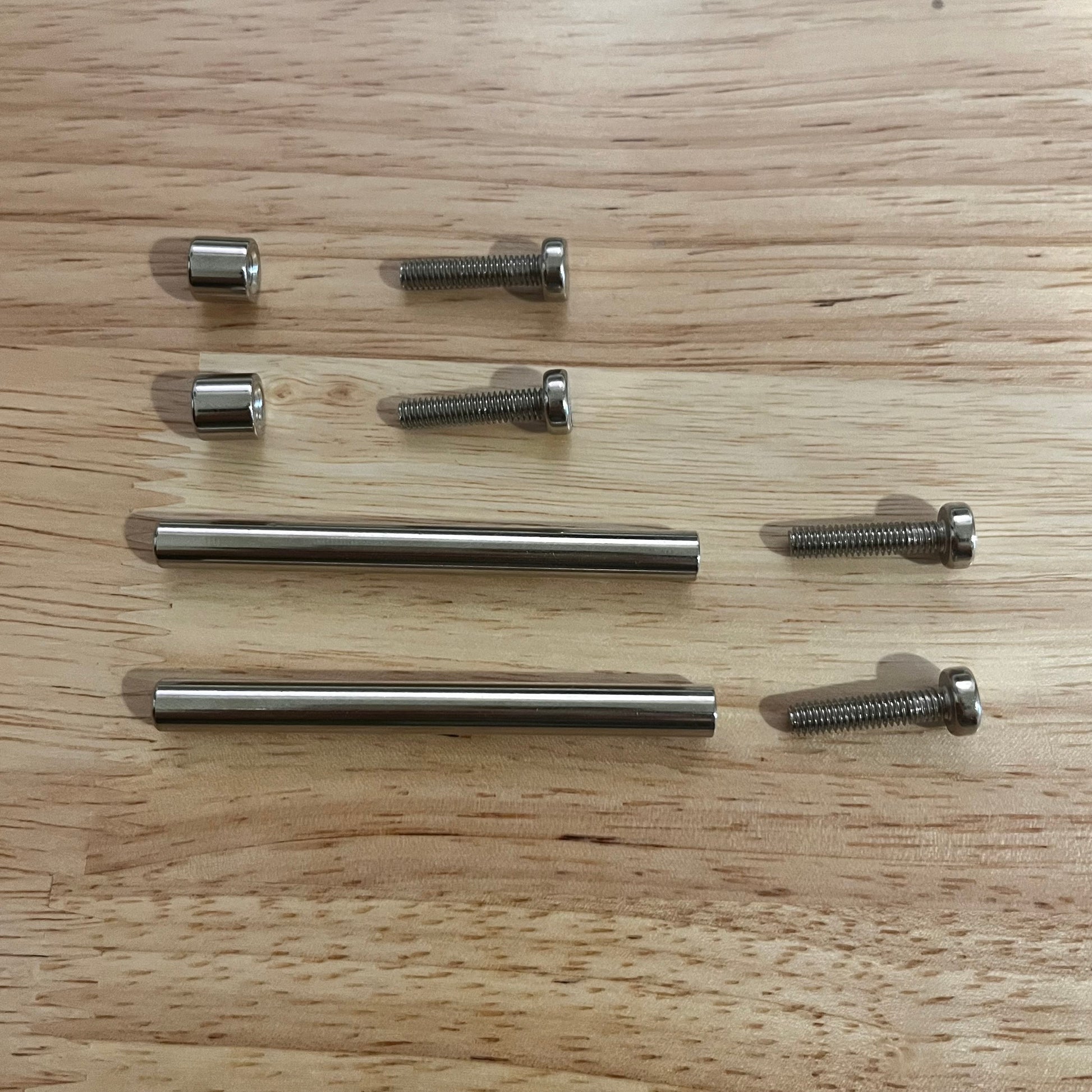 Set of metal screws used to secure acrylic trading card frames on a wooden surface.