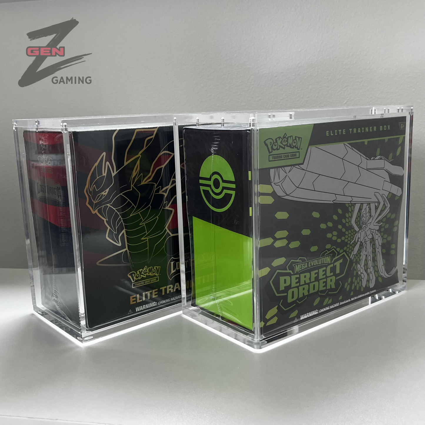 Two clear acrylic display boxes containing Pokémon Elite Trainer Box collectible boxes, shown on a light gray surface against a gray wall. The left box contains a black box with a red and gold dragon illustration, and the right box contains a black box with green and gray spider artwork and a Pokémon logo.
