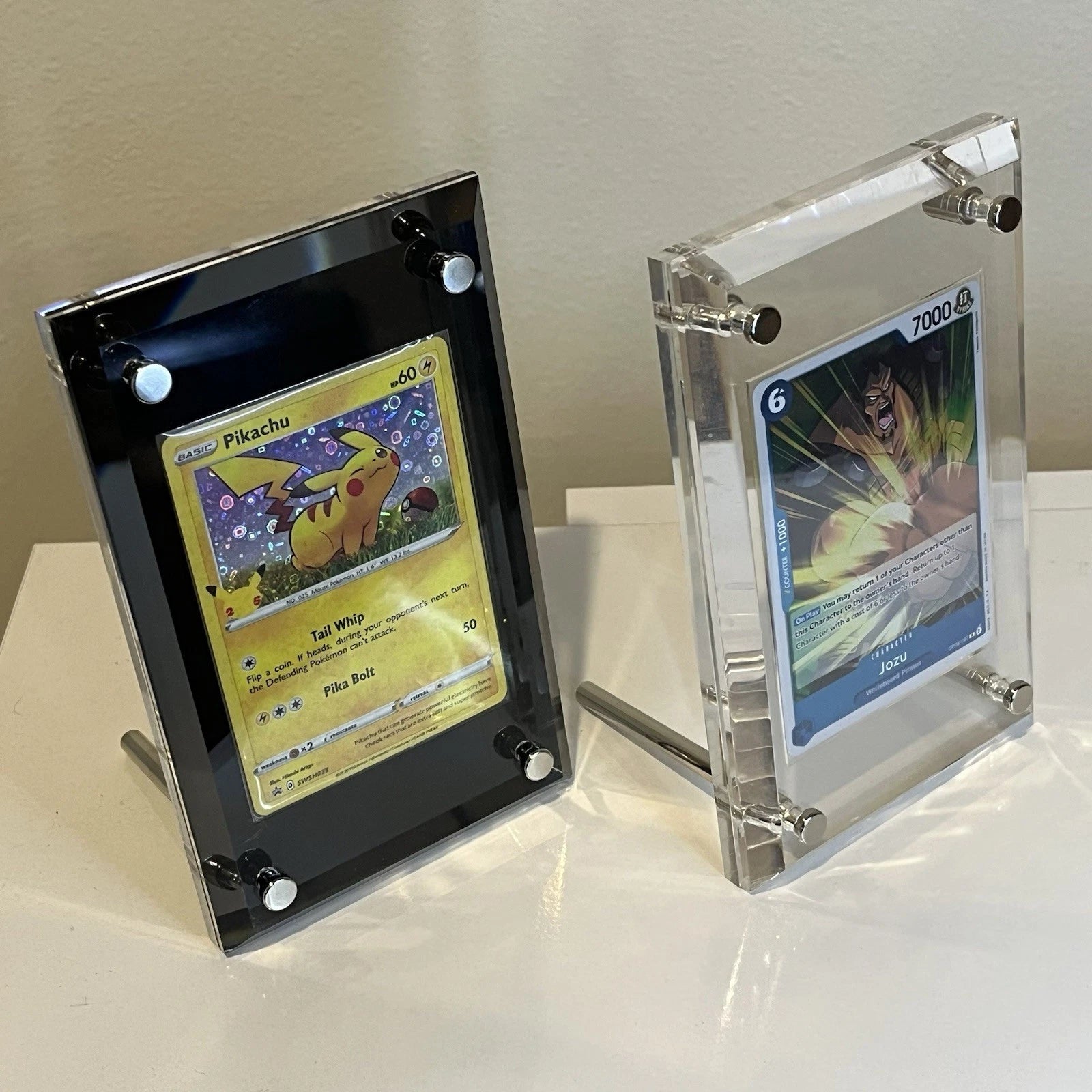 Pokemon and One Piece TCG cards displayed from the side in standing acrylic screwdown cases made for standard size cards. A black and clear screwdown case is shown.
