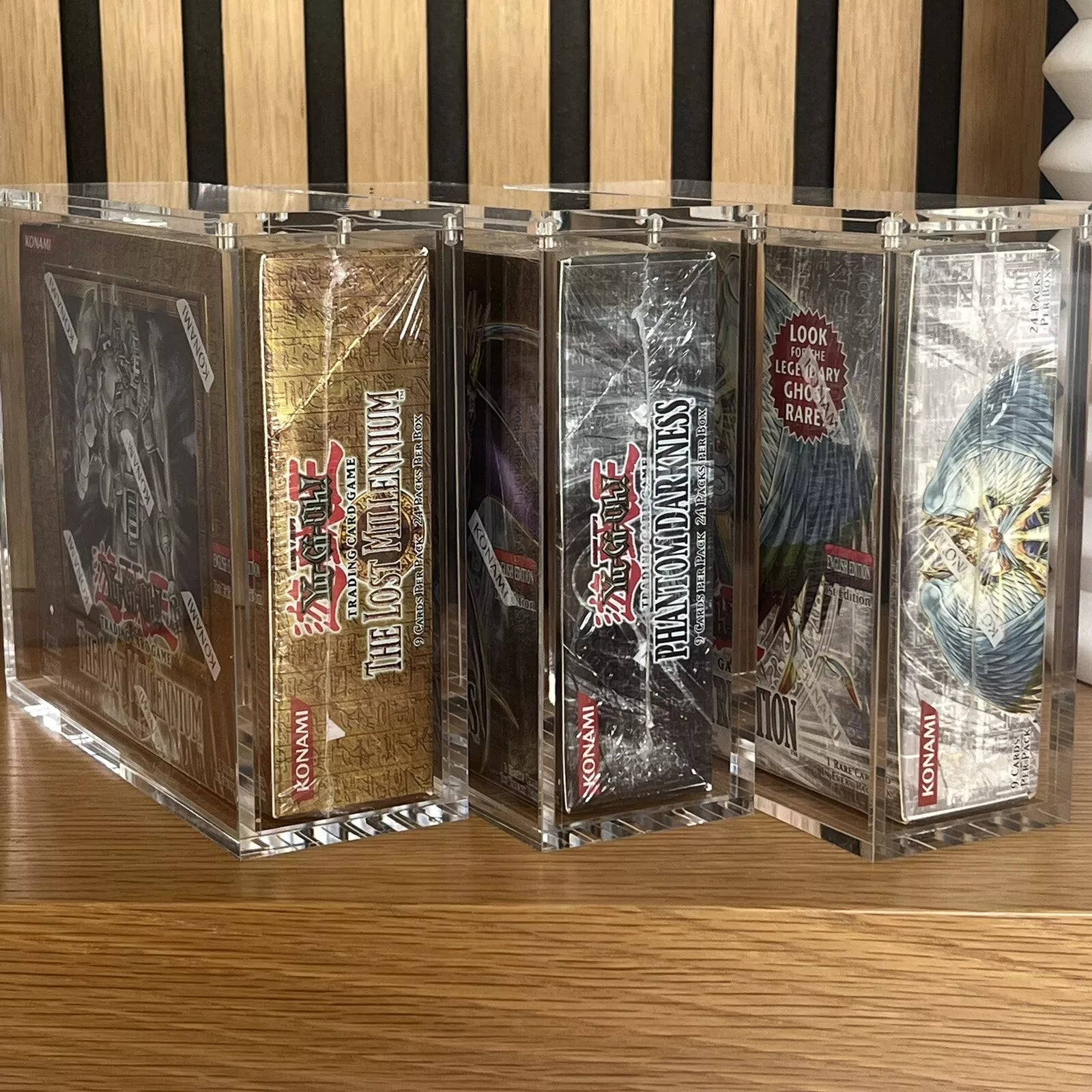 Three vintage yugioh sealed booster boxes in protective acrylic cases on display on a shelf.
