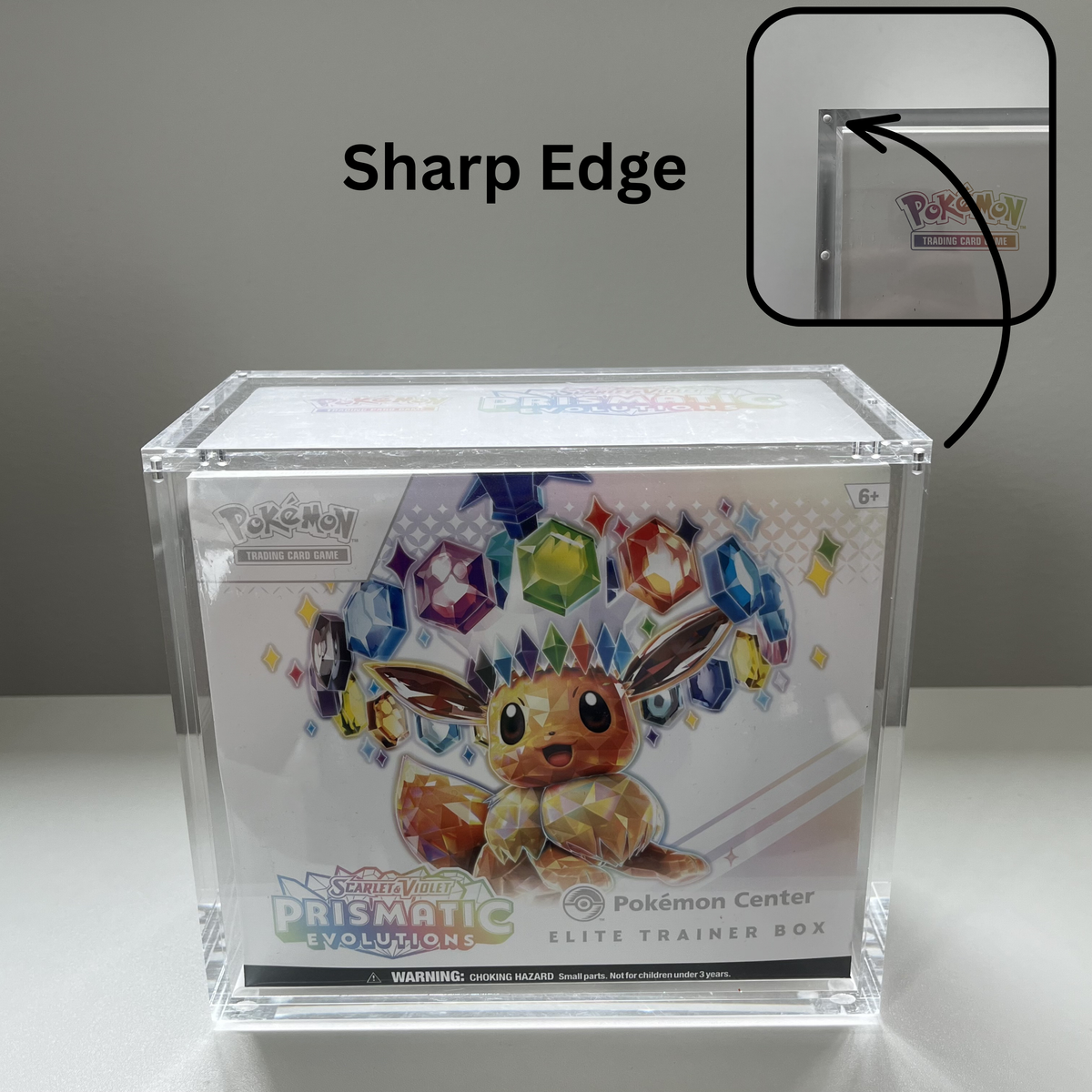A clear acrylic Elite Trainer Box displaying a Pokémon Prismatic Evolutions booster pack, shown on a light gray background with a 'Sharp Edge' callout and inset showing the beveled edge of the acrylic.