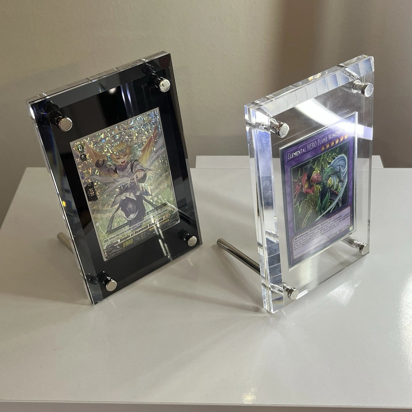 Two acrylic standing screwdown cases one holding a yugioh card the other holding a vanguard card.