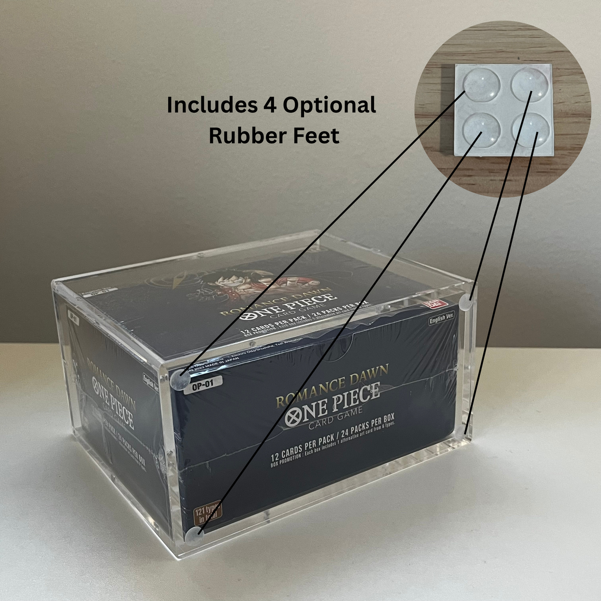 A clear acrylic card display box holding a One Piece trading card booster pack, shown on a light surface against a beige wall. Text reads 'Includes 4 Optional Rubber Feet,' with a circular inset showing the rubber feet and lines pointing to the box corners.