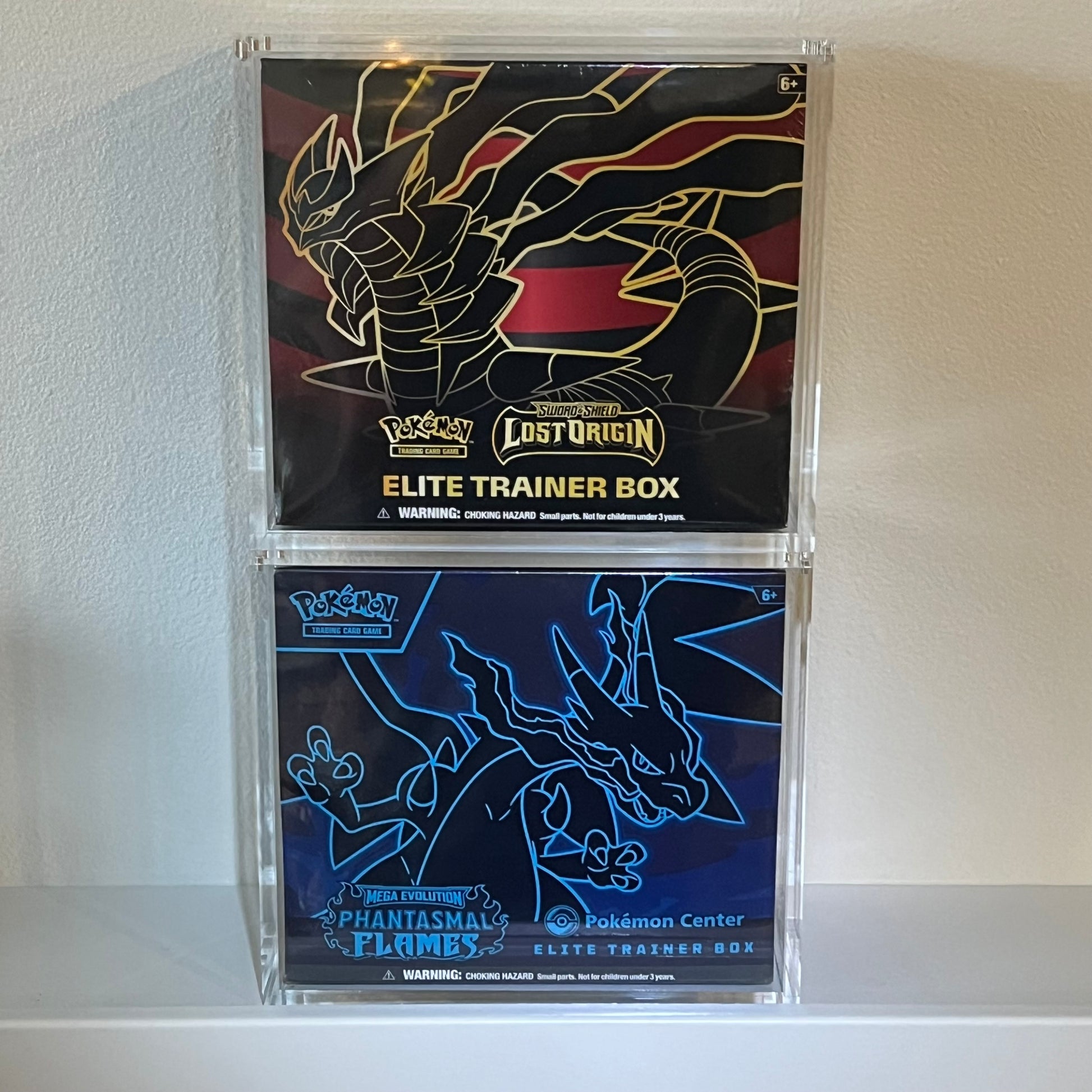 Two Pokémon Elite Trainer Boxes in stackable acrylic display cases.